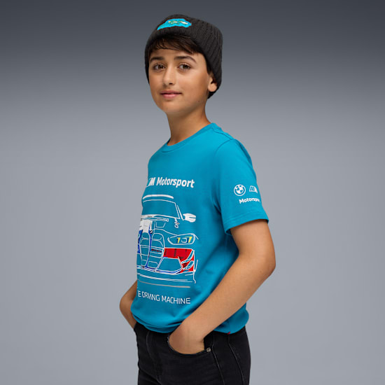 Een model met een grijze muts en blauw Motorsport T-shirt poseert tegen een grijze achtergrond.