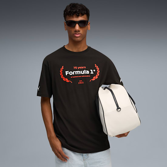 A model holds a bag against a grey backdrop, wearing sunglasses and a Formula 1 logo t-shirt.