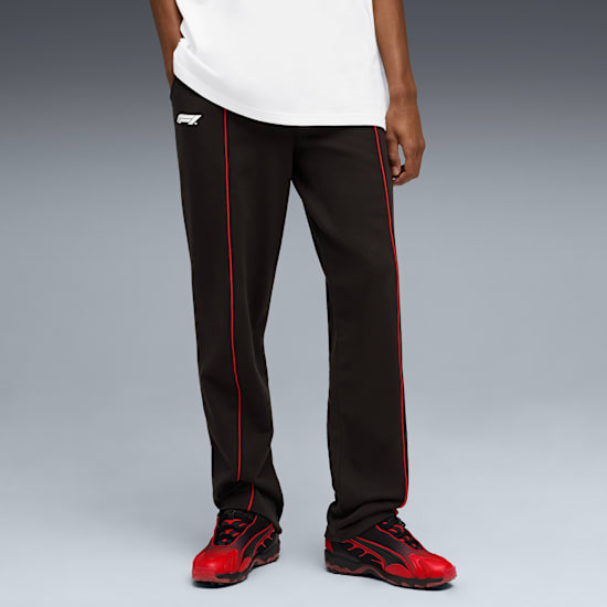 Su sfondo grigio, un modello indossa pantaloni neri con finiture rosse e scarpe da ginnastica rosse.