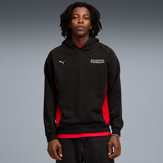 A model stands against grey, wearing a black and red hoodie with dark jeans.