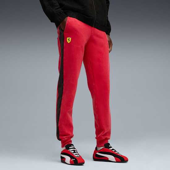 Against grey, a model poses wearing red trousers, shoes and a black jacket.
