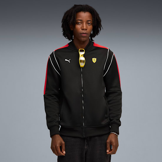 A model stands against grey wearing a black jacket, jeans and yellow sunglasses.