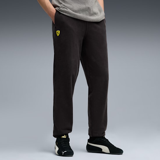 A person stands wearing black trousers with a logo and black and white trainers.