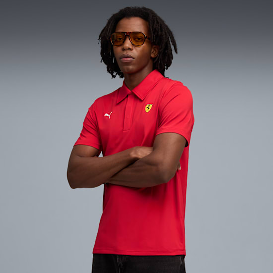 A model with sunglasses in front of a grey background wearing a red polo shirt.