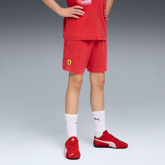 Against grey, a model wears a red t-shirt, shorts, trainers and white socks.