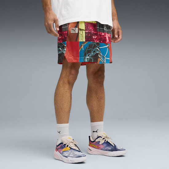 On grey, a model wears a white t-shirt, patterned shorts and colourful running shoes.