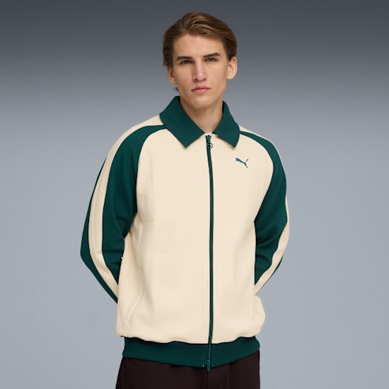 A model poses against a grey backdrop wearing a cream and green zip-up jacket.