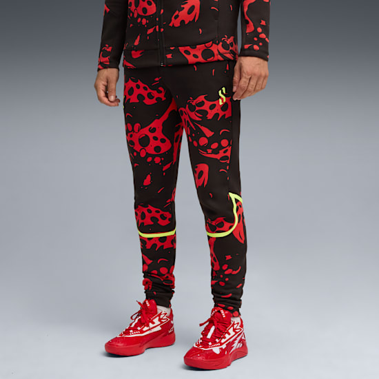 Against grey, a model wears black trousers with red patterns and red trainers.