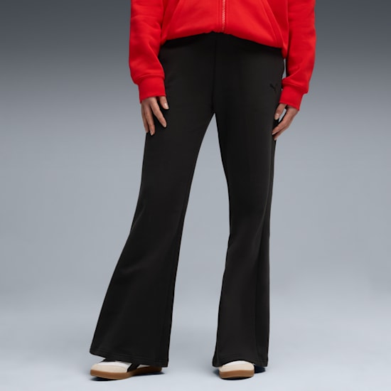 On grey, a model poses wearing black flared trousers, trainers, and a red top.