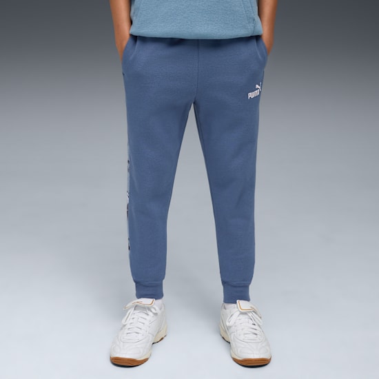 A model stands on a grey background wearing blue joggers and white trainers.