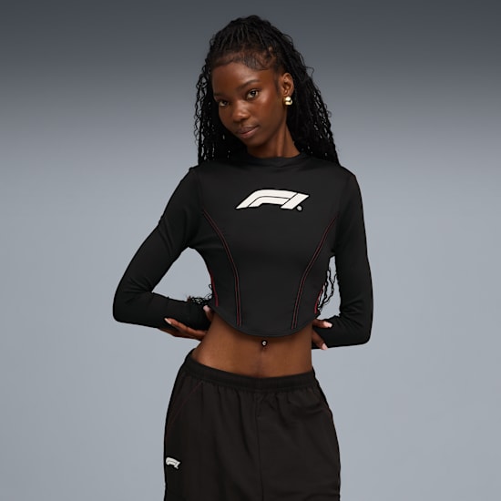 On grey, a model poses in a black top with logo and black shorts.