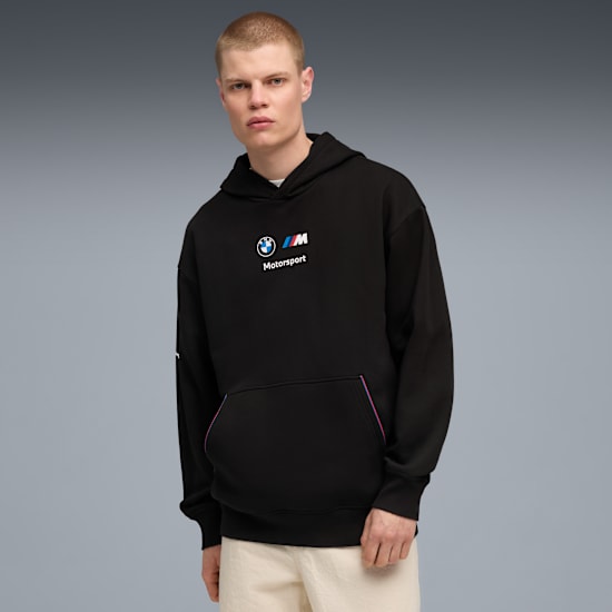 Een model poseert tegen een grijze achtergrond met een zwarte BMW Motorsport hoodie.