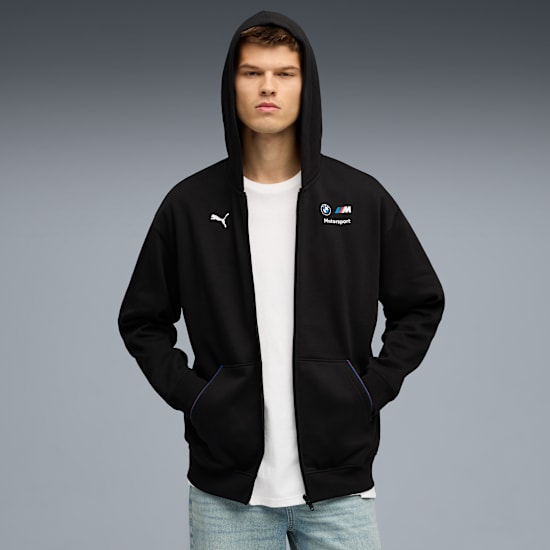 A model poses against grey wearing a black Puma BMW Motorsport hooded jacket.