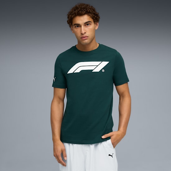 A model in front of a grey background wearing a green t-shirt and white shorts.