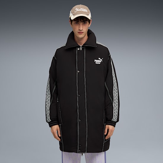 A model stands against grey wearing a cap and a black Puma coat with patterned stripes.