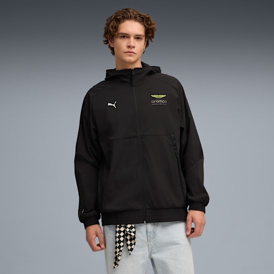 Model pozuje na szarym tle w czarnej markowej kurtce i jasnoniebieskich dżinsach.