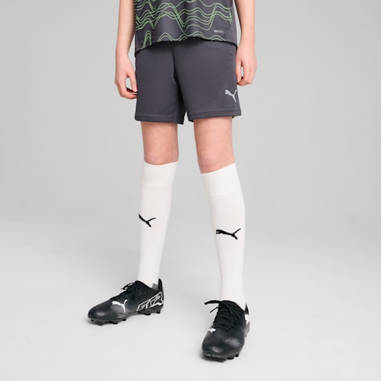 Un modèle se tient sur un fond gris, portant un t-shirt gris, un short, des chaussettes et des chaussures noires.