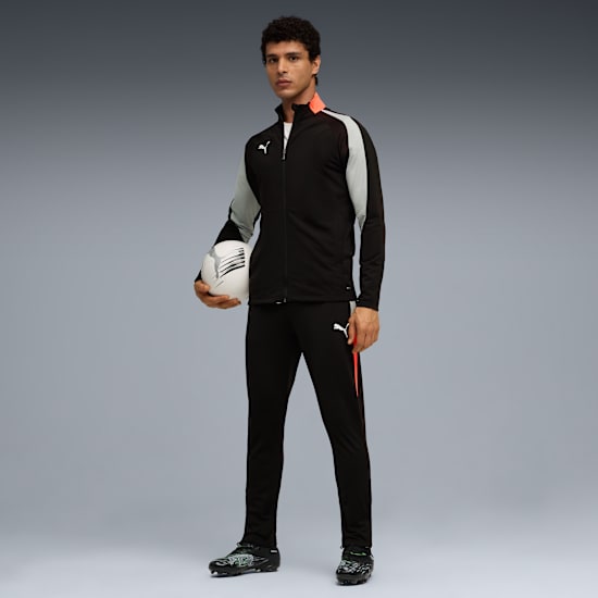 A model stands with a football against a grey background, wearing a black tracksuit.