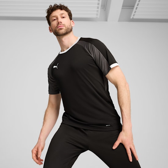 A model poses on a grey backdrop wearing a black t-shirt and black trousers.