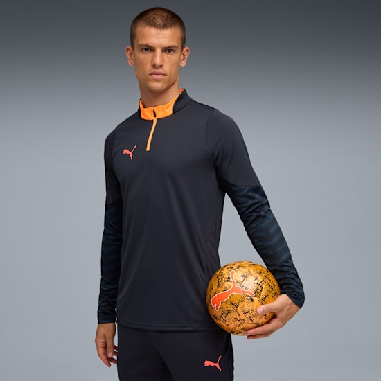 Model poses with a ball against a grey backdrop, wearing a dark top and trousers.