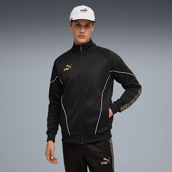 A model stands on a grey backdrop, wearing a cap, black jacket and trousers.