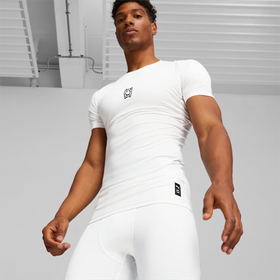 Een model staat tegen een neutrale achtergrond, gekleed in een wit T-shirt en witte legging.