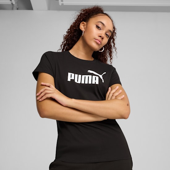Een model poseert met gekruiste armen op een grijze achtergrond in een zwart Puma T-shirt.