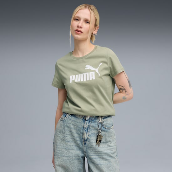 A model poses against a grey backdrop, wearing a light green logo t-shirt and jeans.