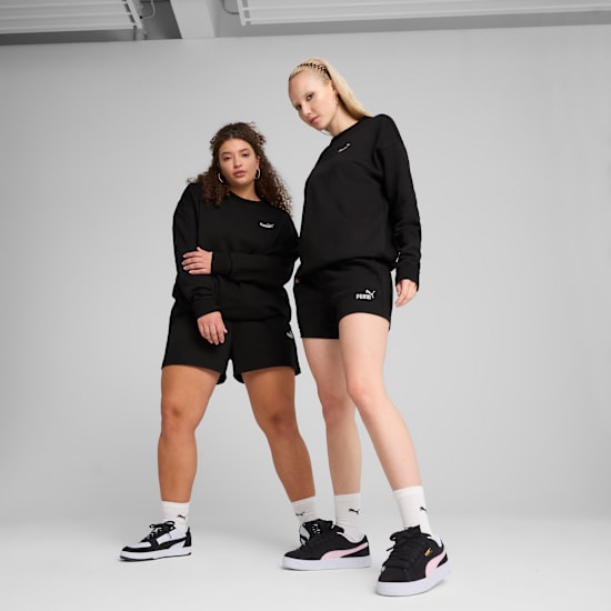 Two models pose against a grey backdrop wearing black sweatshirts, shorts, and trainers.
