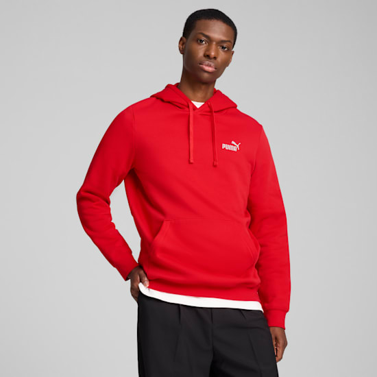A model poses against grey, wearing a red hoodie and black trousers.