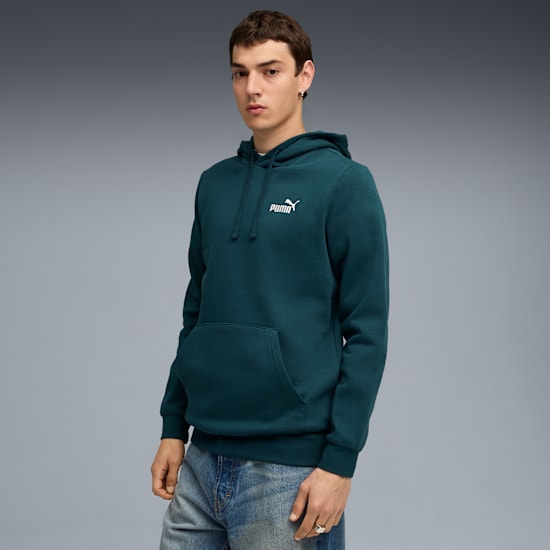 Een model poseert tegen een grijze achtergrond, gekleed in een blauwgroene hoodie met wit logo.
