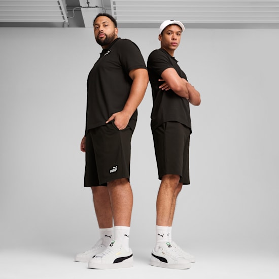 Due modelli in piedi schiena contro schiena su sfondo grigio, con top neri, pantaloncini e scarpe da ginnastica bianche.