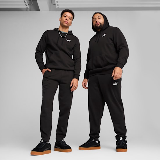 Two models pose on a grey backdrop wearing black tracksuits and trainers.