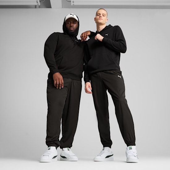 Two models pose in front of a grey background wearing black hoodies, trousers and white trainers.
