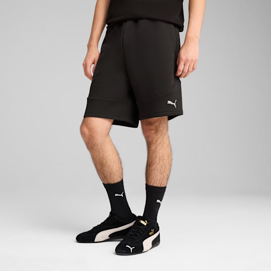 On grey, a model wears black shorts, socks, and shoes with a white logo.