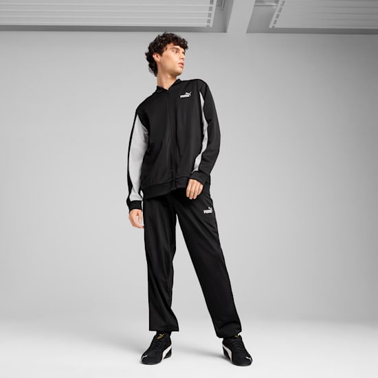 A model poses against a grey backdrop, wearing a black Puma tracksuit and trainers.