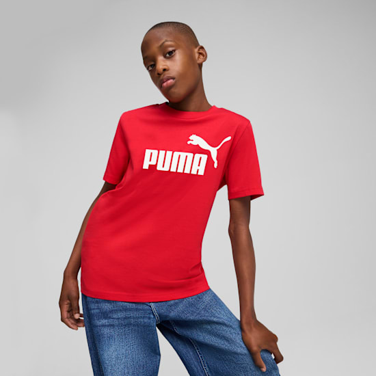 Een model poseert tegen een grijze achtergrond, met een rood Puma T-shirt en blauwe jeans.