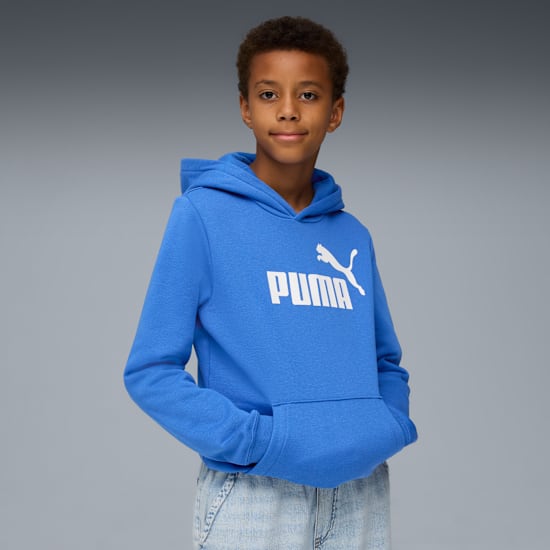 Un modèle pose sur un fond gris, portant un sweat à capuche bleu avec un logo Puma blanc.
