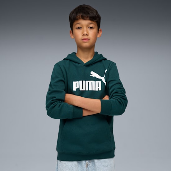 A child poses against a grey backdrop, wearing a green hoodie with a white Puma logo.