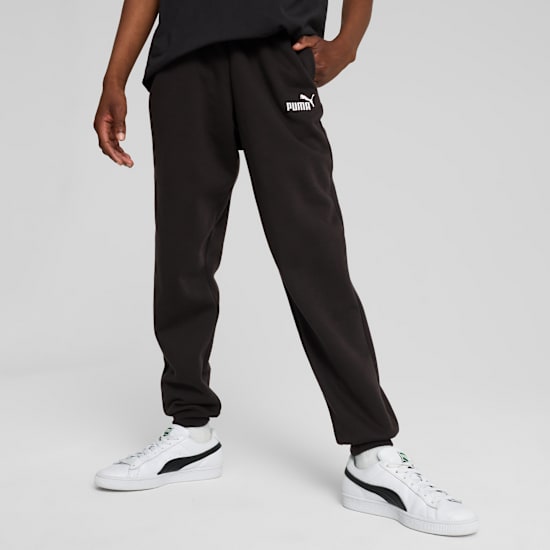 A model poses on a grey background wearing black sweatpants and white trainers.