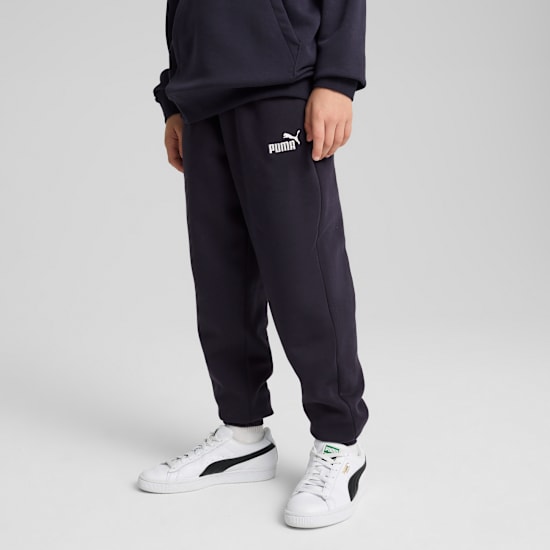 Een model staat op een grijze achtergrond, gekleed in een marineblauwe joggingbroek en witte sneakers.