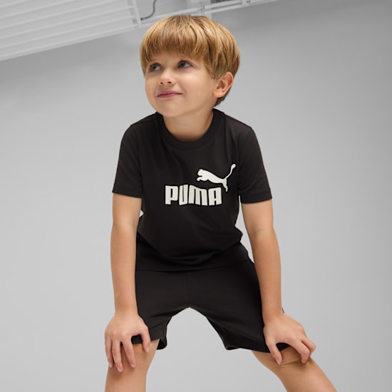 Sur fond gris, un enfant blond porte un t-shirt et un short Puma noirs, regardant vers le haut.