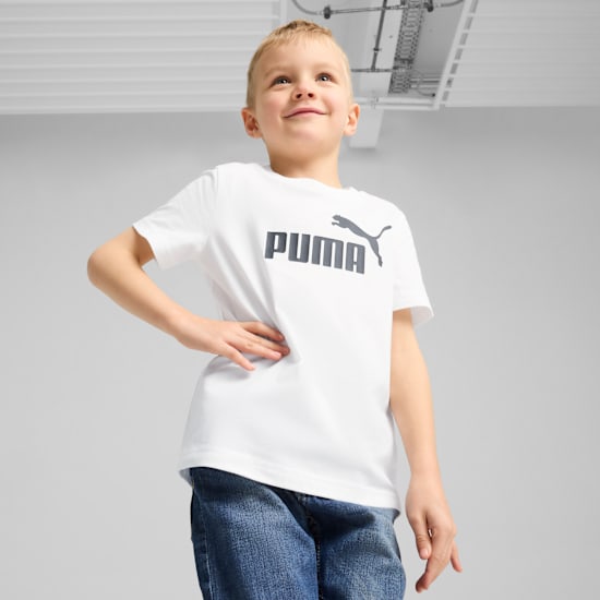 A boy poses against a grey backdrop wearing a white Puma t-shirt and blue jeans.