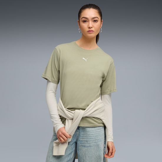 A model poses against a grey backdrop, wearing a green t-shirt, jeans, and a tied jumper.