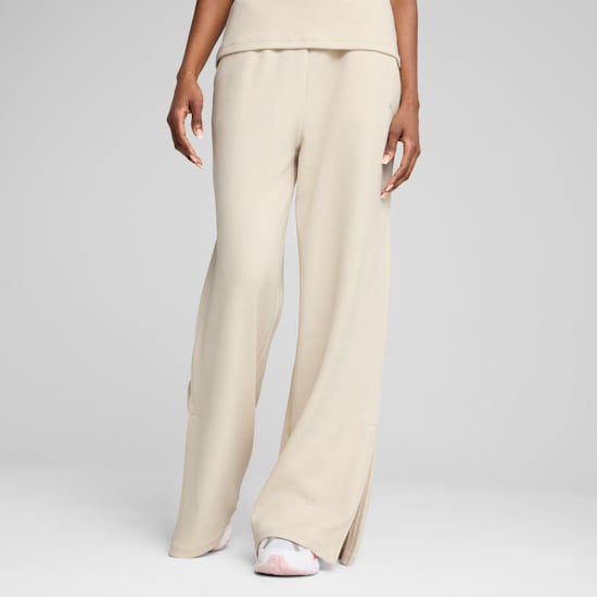 Against grey, a model poses in cream, wide-leg trousers and trainers, mid-stride.