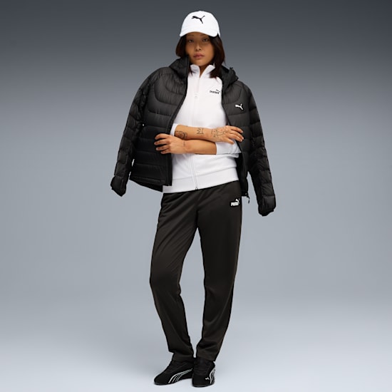 Model ze skrzyżowanymi rękami stoi na szarym tle, ubrany w biały top, kurtkę i ciemne spodnie.