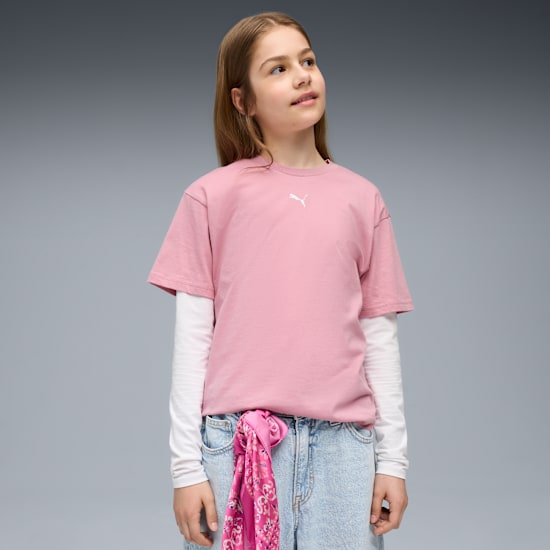 Ein Model posiert vor grauem Hintergrund mit rosa T-Shirt, Jeans und Schal.