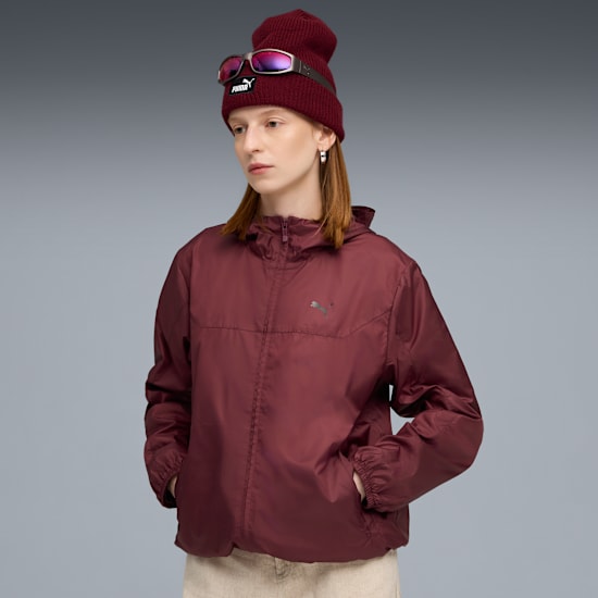 A model in a maroon jacket, beanie and goggles poses against a grey background.