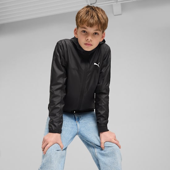 Against a grey backdrop, a model poses in a black jacket and light blue jeans.