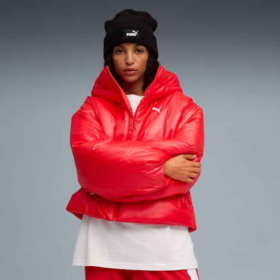 Against grey, a model with crossed arms wears a red puffer jacket and black beanie.